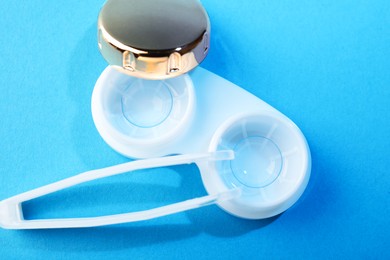 Photo of Contact lenses in case and tweezers on blue background, flat lay