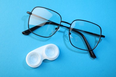 Photo of Contact lenses in case and glasses on blue background, flat lay
