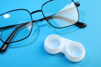 Photo of Contact lenses in case and glasses on blue background, closeup