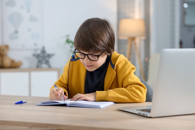 Photo of Cute little boy doing homework at table indoors