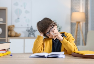 Photo of Cute little boy doing homework at table indoors