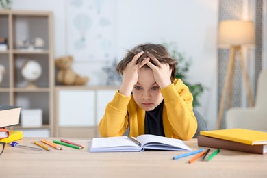 Photo of Tired little boy doing homework at table indoors