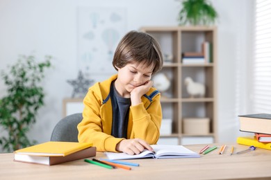 Photo of Cute little boy doing homework at table indoors