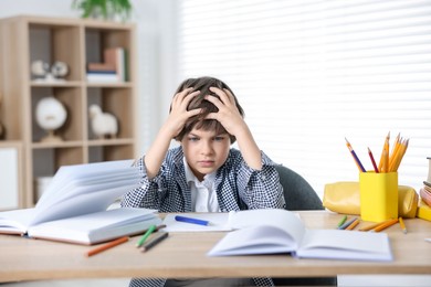 Photo of Tired little boy doing homework at table indoors
