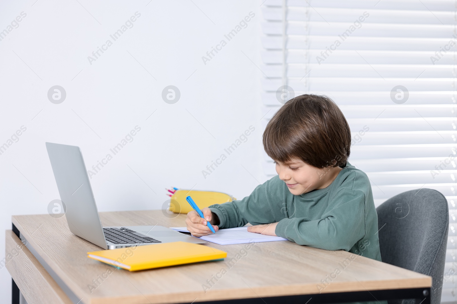 Cute little boy doing homework at table indoors Photo of Cute little boy doing homework at table indoors