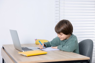 Photo of Cute little boy doing homework at table indoors