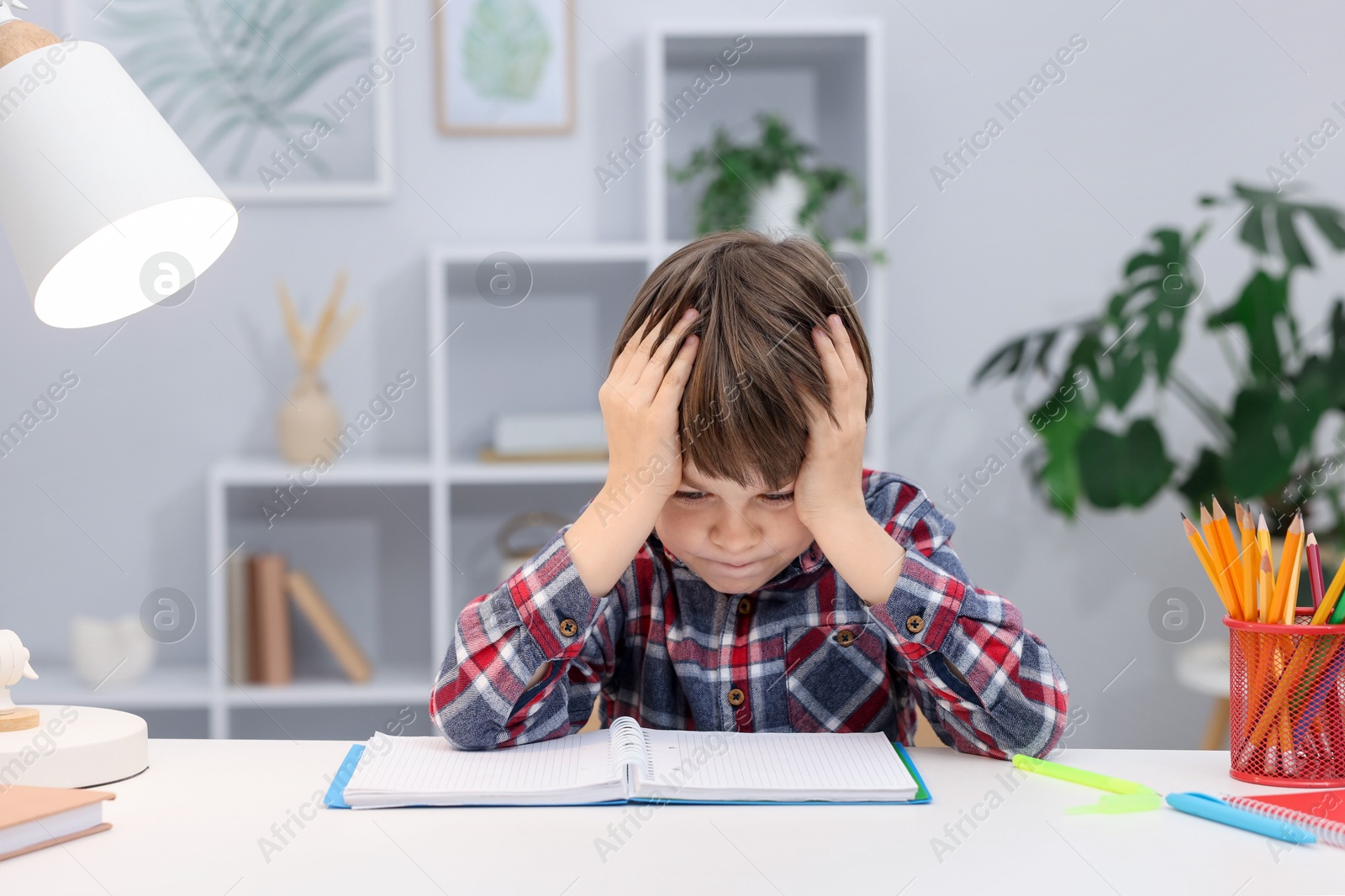 Tired little boy doing homework at desk indoors Photo of Tired little boy doing homework at desk indoors