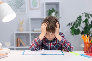 Photo of Tired little boy doing homework at desk indoors