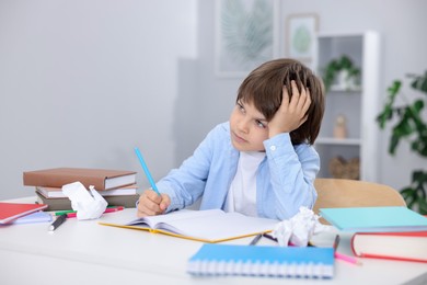 Photo of Tired little boy doing homework at table indoors