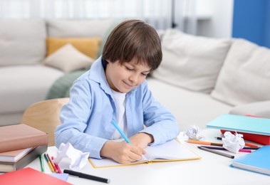 Photo of Cute little boy doing homework at table indoors