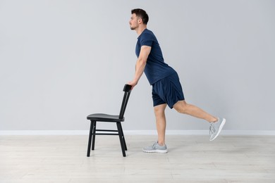 Photo of Handsome man exercising with chair at home