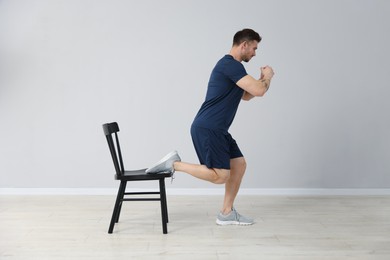 Photo of Handsome man exercising with chair at home