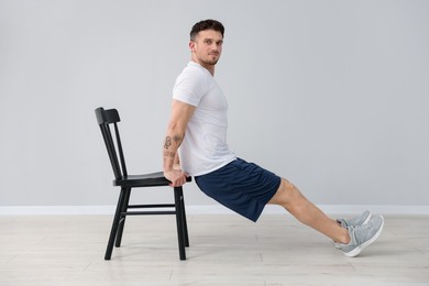 Photo of Handsome man exercising with chair at home