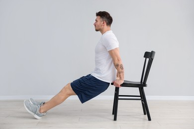 Photo of Handsome man exercising with chair at home