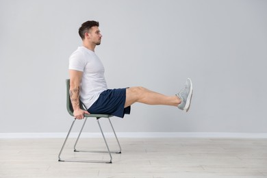 Photo of Handsome man exercising with chair at home