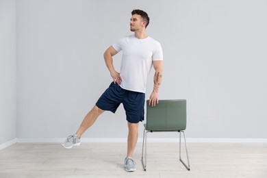 Photo of Handsome man exercising with chair at home