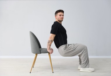 Photo of Handsome man exercising with chair at home