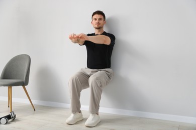 Photo of Handsome man exercising near light grey wall indoors