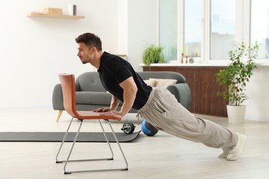 Photo of Handsome man exercising with chair at home
