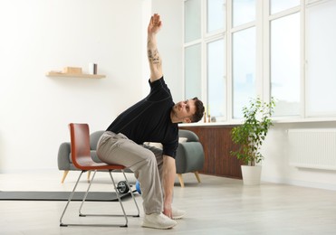 Photo of Handsome man exercising with chair at home