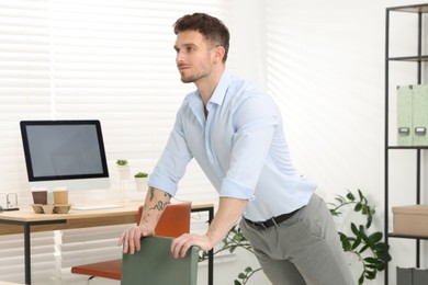 Photo of Handsome man exercising with chair in office