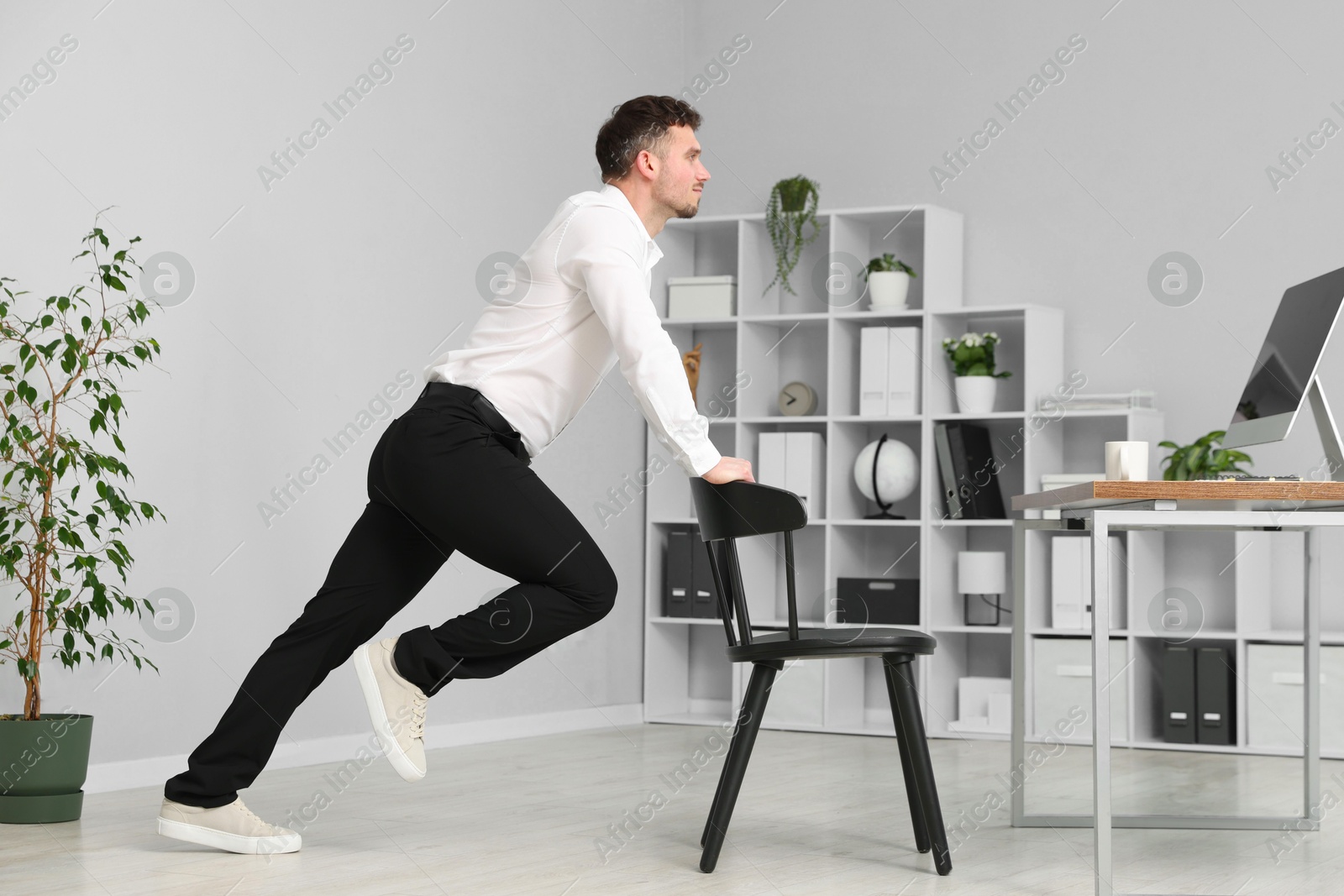 Handsome man exercising with chair in office Photo of Handsome man exercising with chair in office