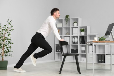 Photo of Handsome man exercising with chair in office