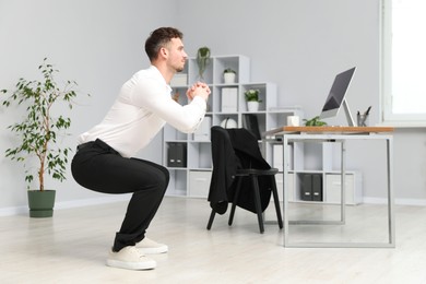 Photo of Handsome man doing exercise near desk in office