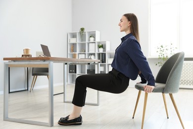 Photo of Beautiful woman exercising with chair in office