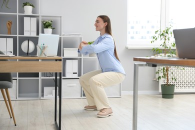 Photo of Beautiful woman doing exercise near desk in office