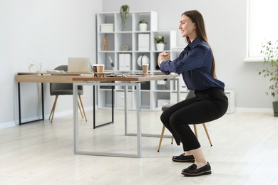 Photo of Beautiful woman doing exercise near desk in office