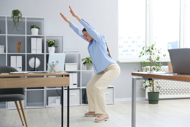 Photo of Beautiful woman doing exercise near desk in office