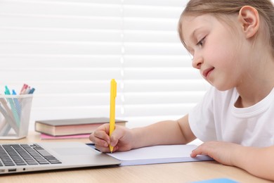 Photo of Little girl doing homework at table indoors