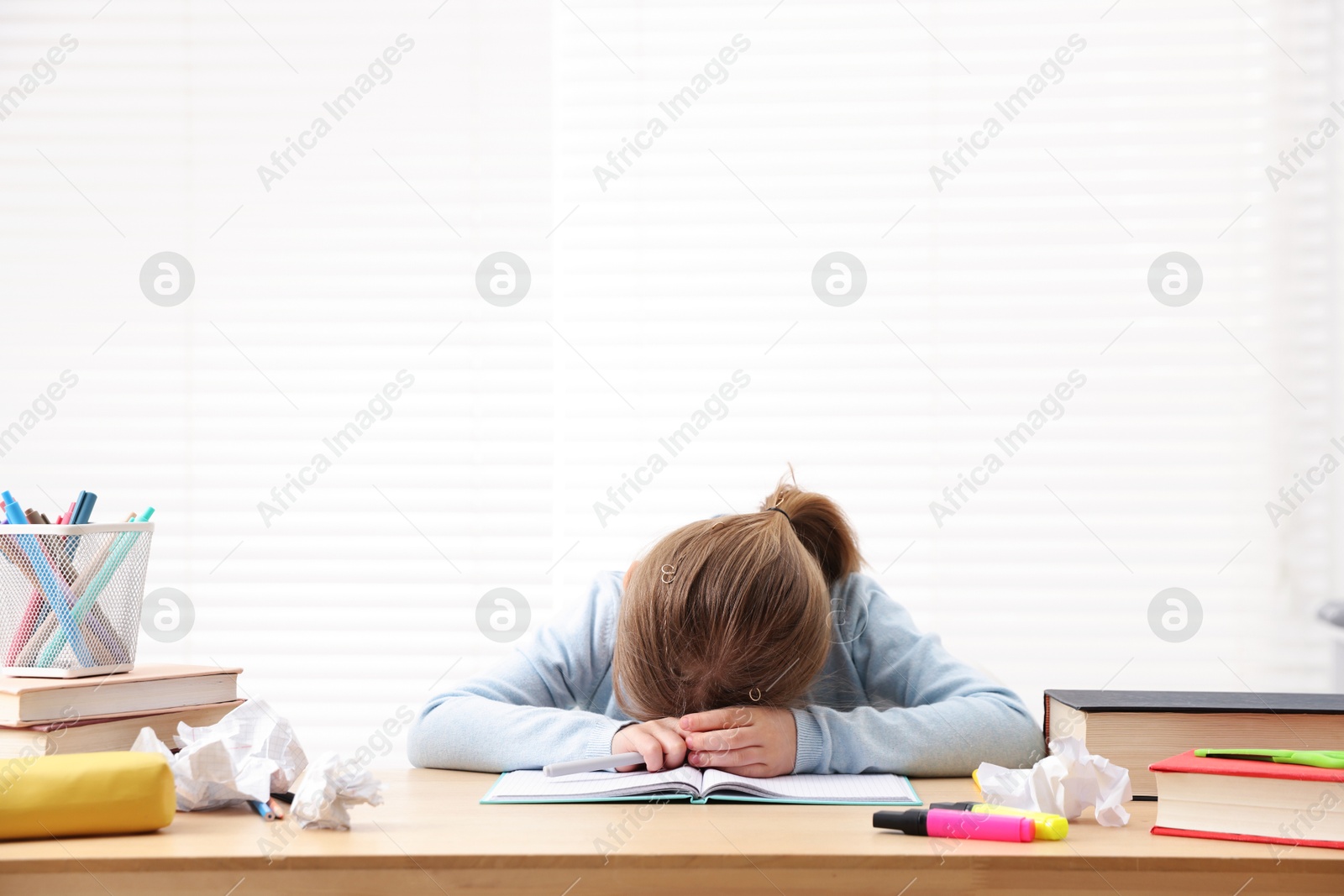 Tired little girl doing homework at table indoors Photo of Tired little girl doing homework at table indoors