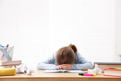 Photo of Tired little girl doing homework at table indoors