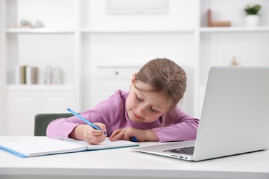 Photo of Little girl doing homework at table indoors