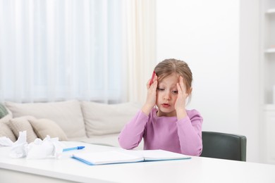 Photo of Tired little girl doing homework at table indoors, space for text