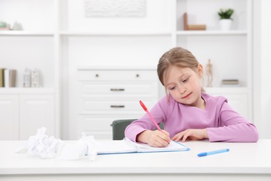 Photo of Little girl doing homework at table indoors, space for text