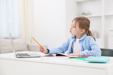Photo of Little girl doing homework at table indoors