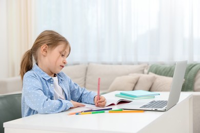 Photo of Little girl doing homework at table indoors