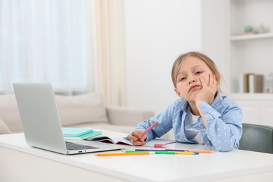 Photo of Tired little girl doing homework at table indoors
