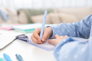 Photo of Little girl doing homework at table indoors, closeup