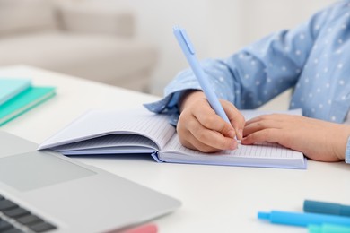 Photo of Little girl doing homework at table indoors, closeup