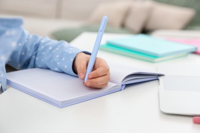Photo of Little girl doing homework at table indoors, closeup