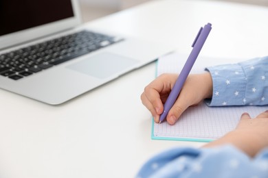 Photo of Little girl doing homework at table indoors, closeup