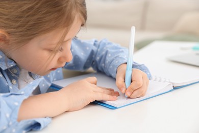 Photo of Little girl doing homework at table indoors