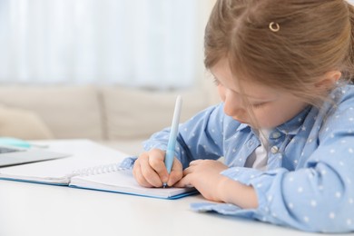 Photo of Little girl doing homework at table indoors