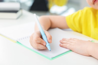 Photo of Little girl doing homework at table indoors, closeup