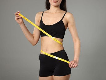 Photo of Woman with slim body and measuring tape on gray background, closeup