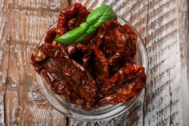 Photo of Delicious sun dried tomatoes with basil in glass bowl on wooden table, top view